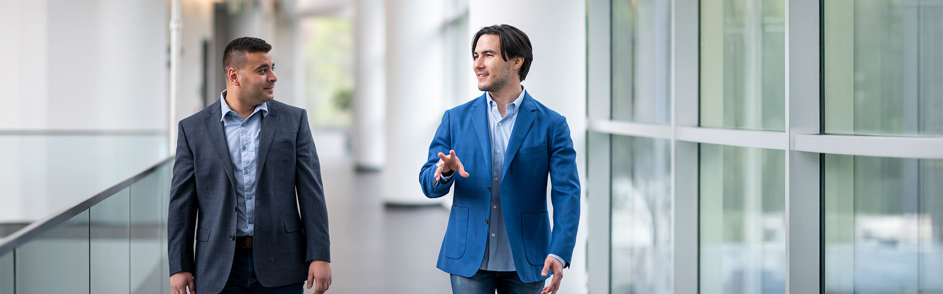 Two male students walk and talk on the atrium walkway in Scheller