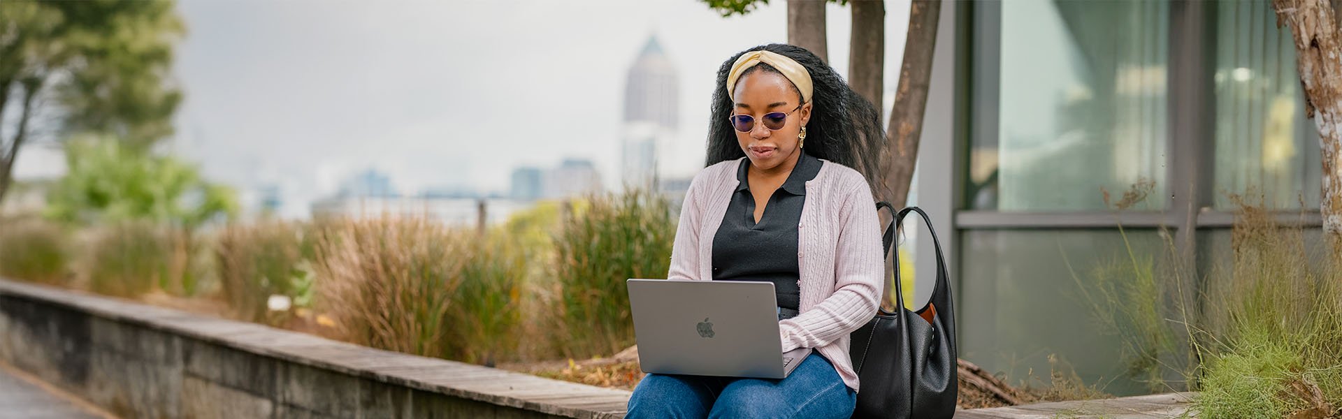 Female Scheller student in sunglasses on laptop outside