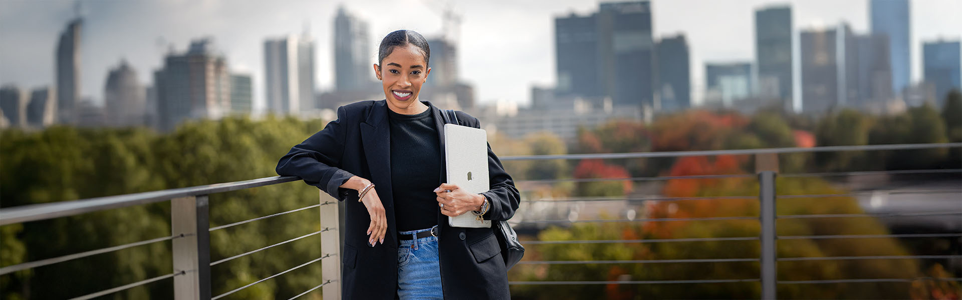 Female Scheller student on rooftop railing with laptop posing for camera