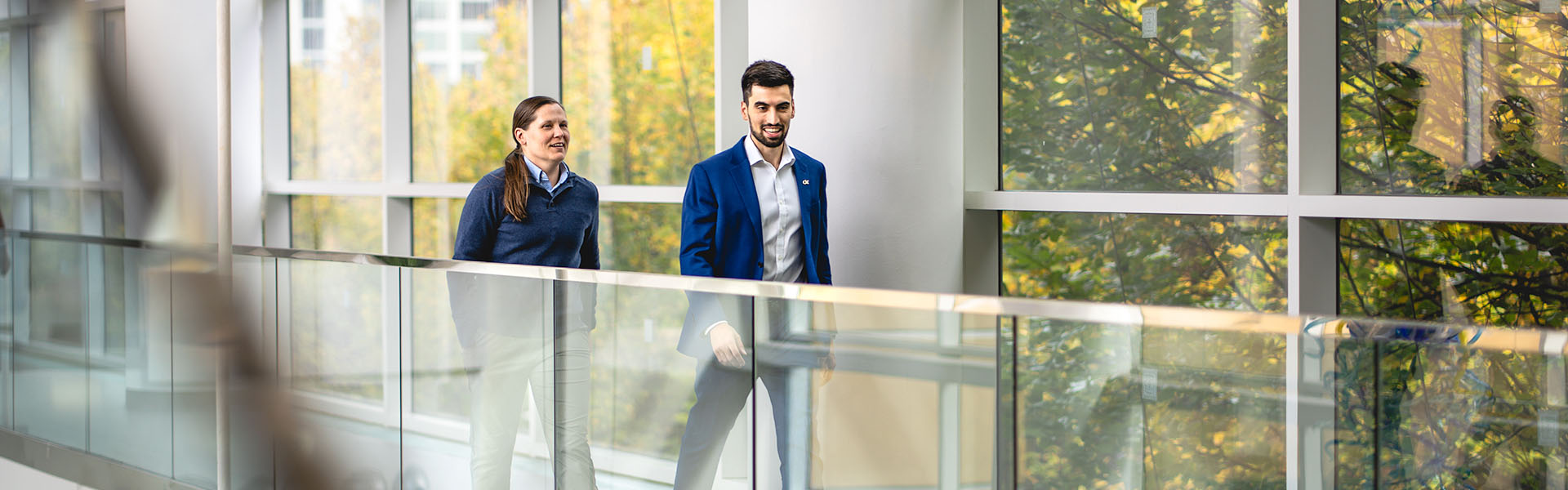 One male and one female MBA student walking across atrium bridge chatting