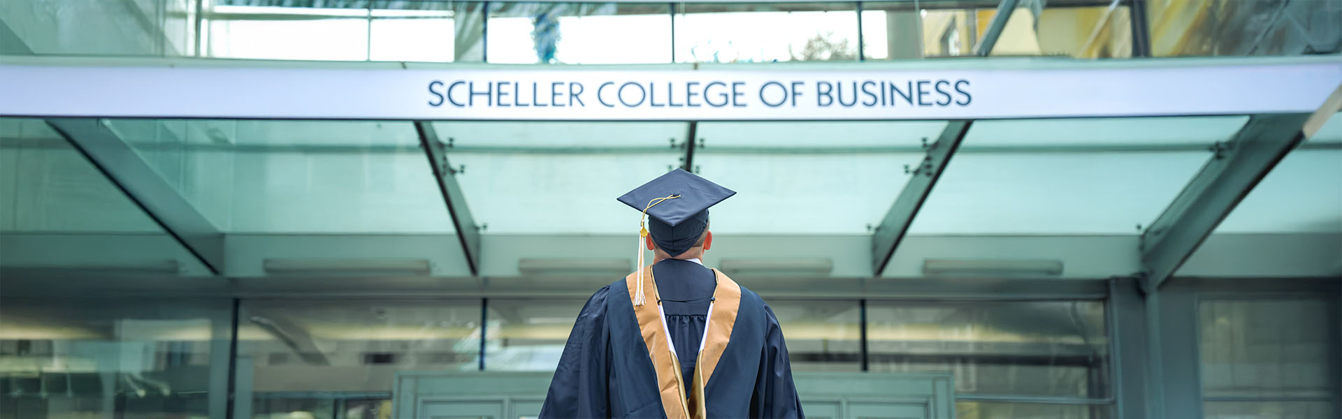 MBA student in graduation cap and gown, back to the camera, looking at Scheller building entrance