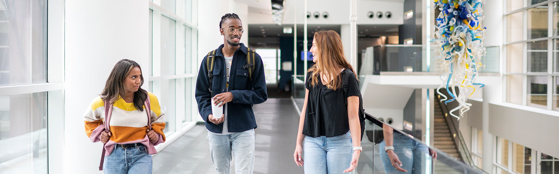 Three student walking across Scheller atrium bridge