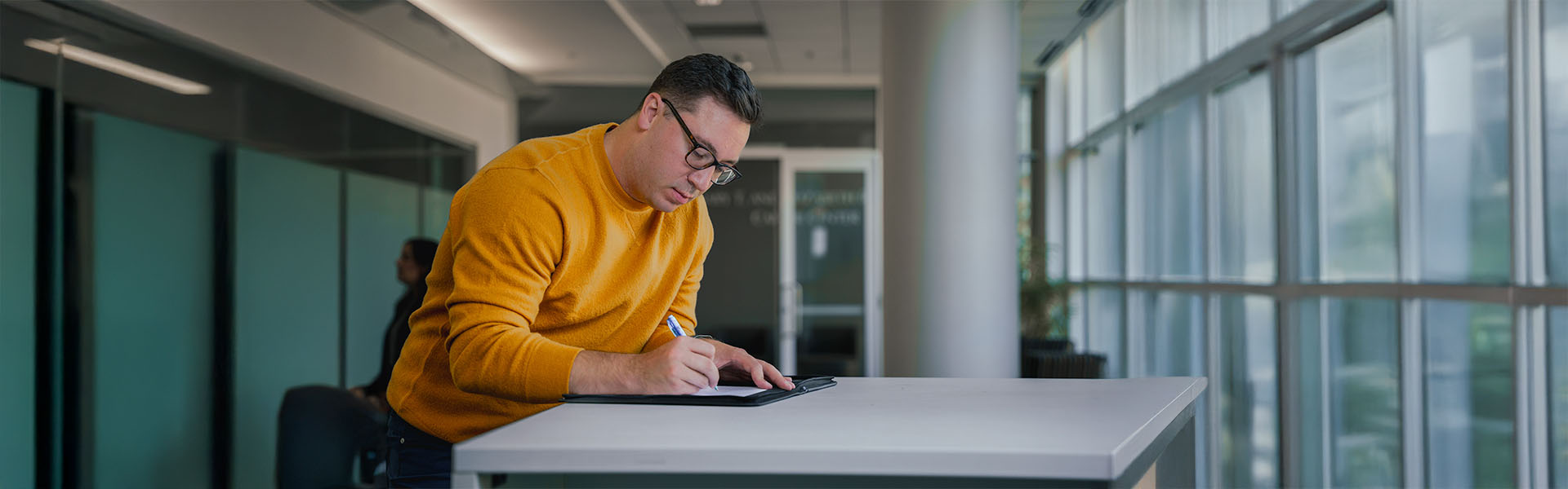 Male MBA student writing in notebook, standing at high-top table