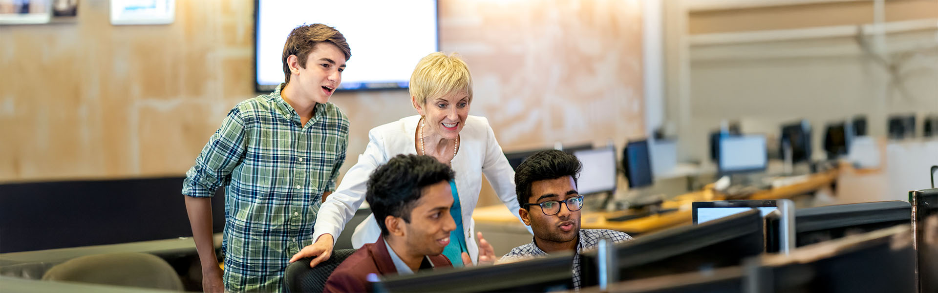 Faculty member and 3 undergraduate students gather around computer lab