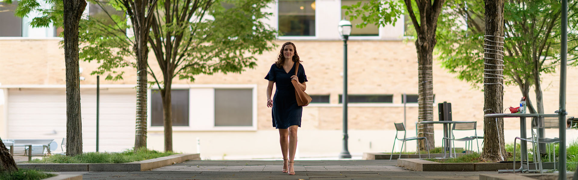 Female undergraduate student walks under tree covered sidewalk in front of Scheller building