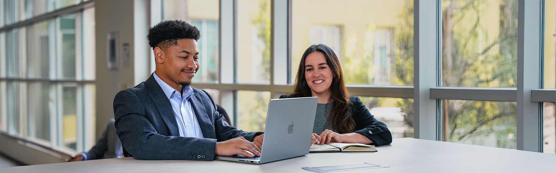 Two students working on laptop inside Scheller on high-top table smiling