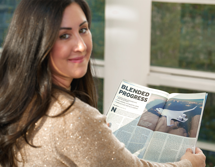 A dark haired woman looks over her shoulder holding out a magazine