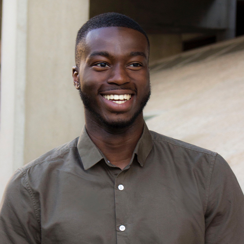 A man wearing a dark green button up shirt smiles