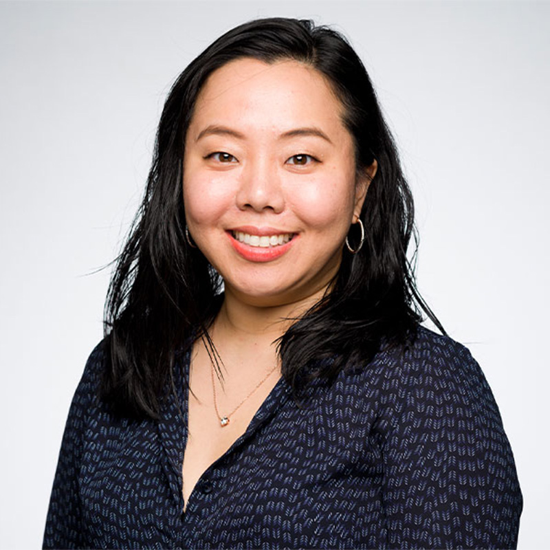 A woman with dark hair smiles at the camera wearing a dark button up shirt