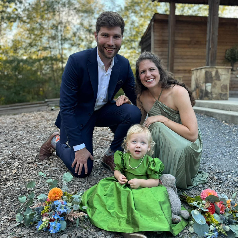 A man and woman pose for a photo with a little girl dressed in a green dress