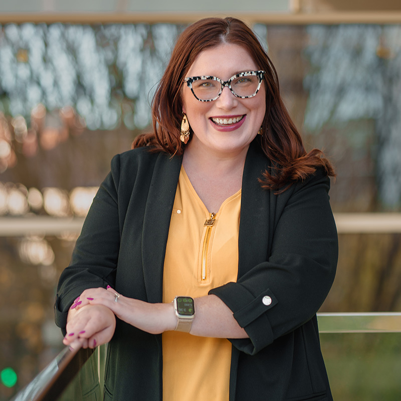 A woman in thick framed glasses smiles outdoors