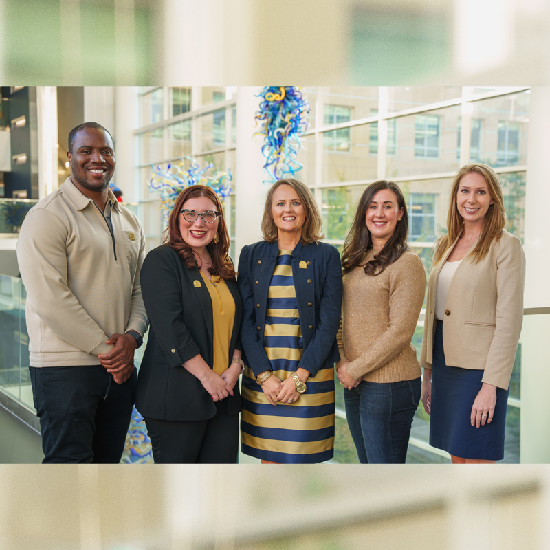 One man and four women stand in the Scheller College of Business atrium dressed in Georgia Tech navy and gold 