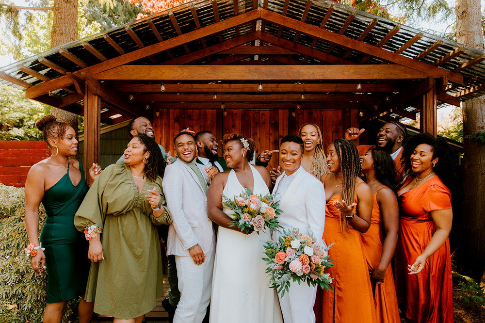 Two women stand in white surrounded by family and friends