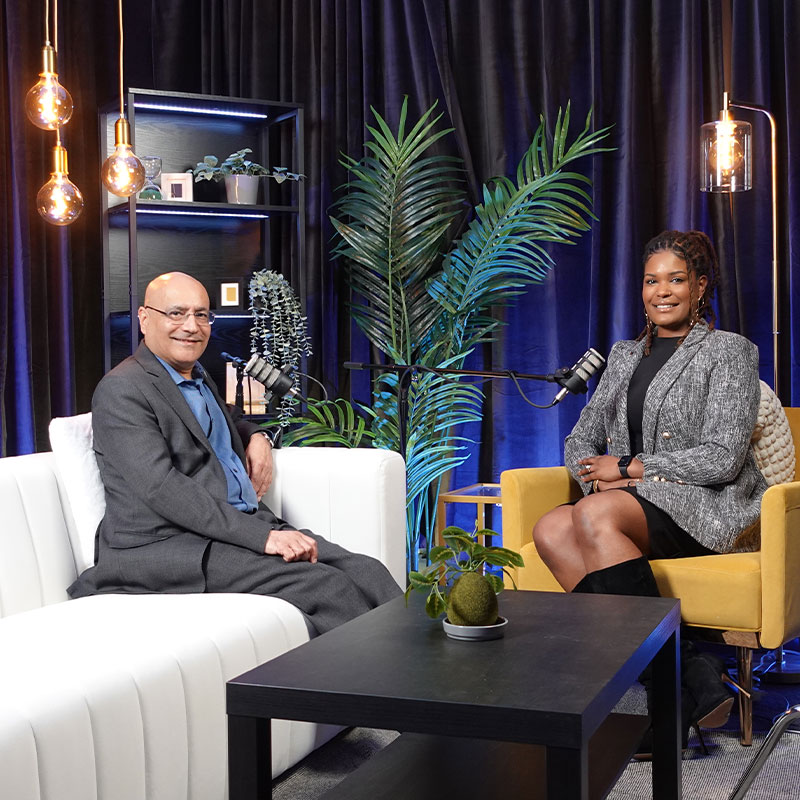 Dean Anuj Mehrotra and MBA student Analisa Wade sit in a room with microphones to record a podcast 