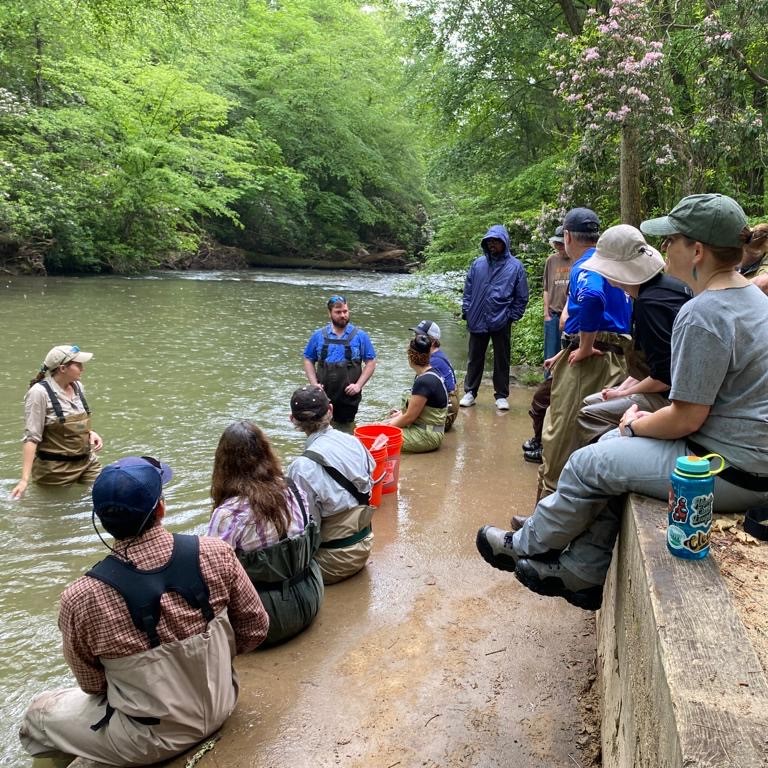 People gathered in an outdoor classroom at a river. 